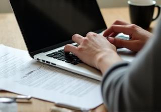 Hands typing on a laptop with script pages